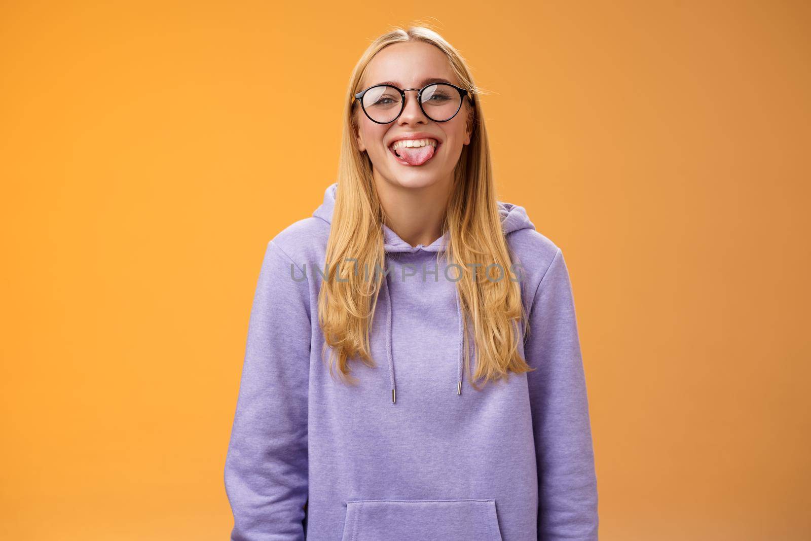 Funny charming female programmer having fun show tongue fool around coworkers during lunch break smiling broadly laughing in cute glasses purple hoodie, standing purple background.