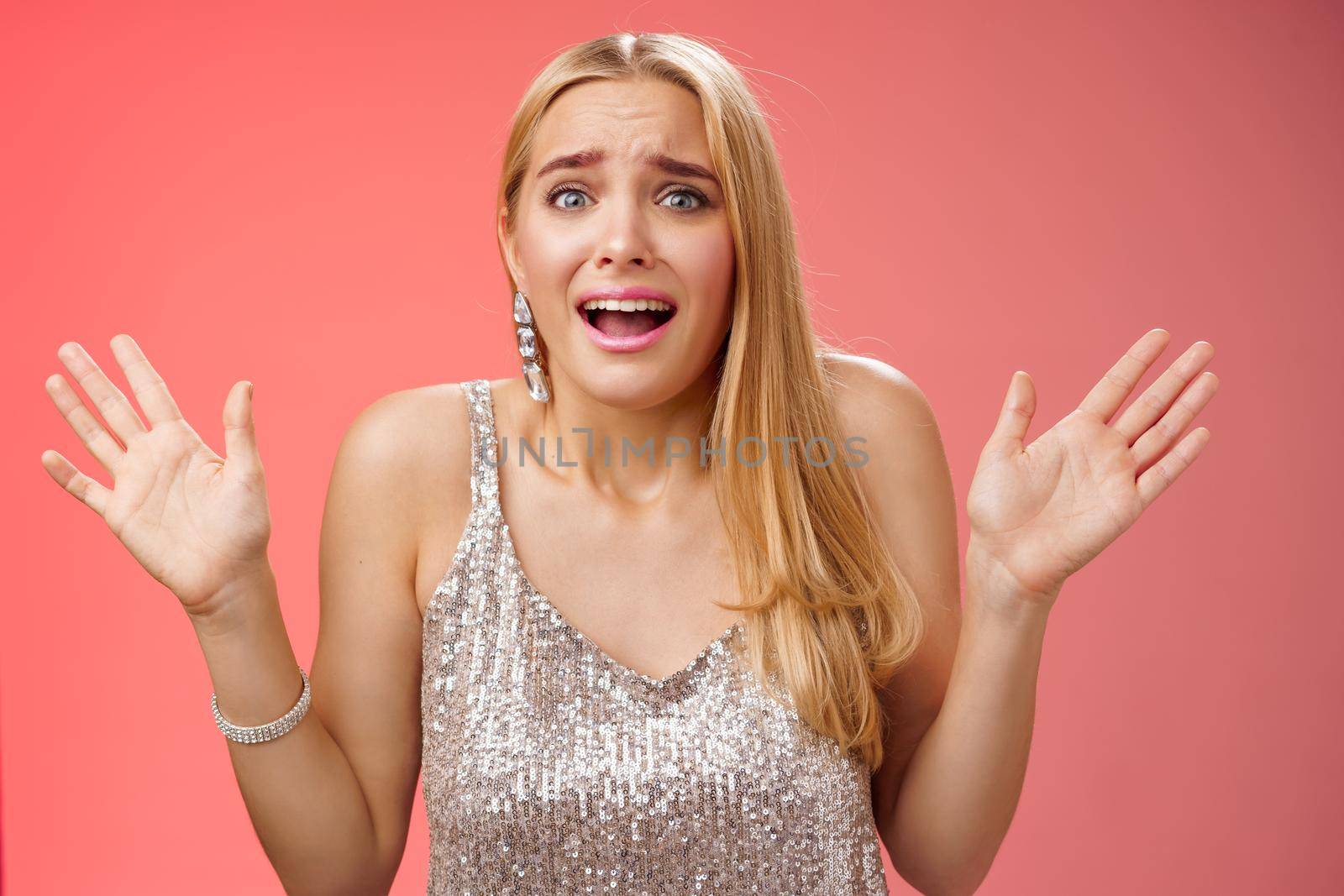 Lifestyle. Freaked-out nervous young girl worry party not go well panicking gesturing raised hands worried frowning grimacing complaining friends feel unconfident unsure standing silver dress red background.