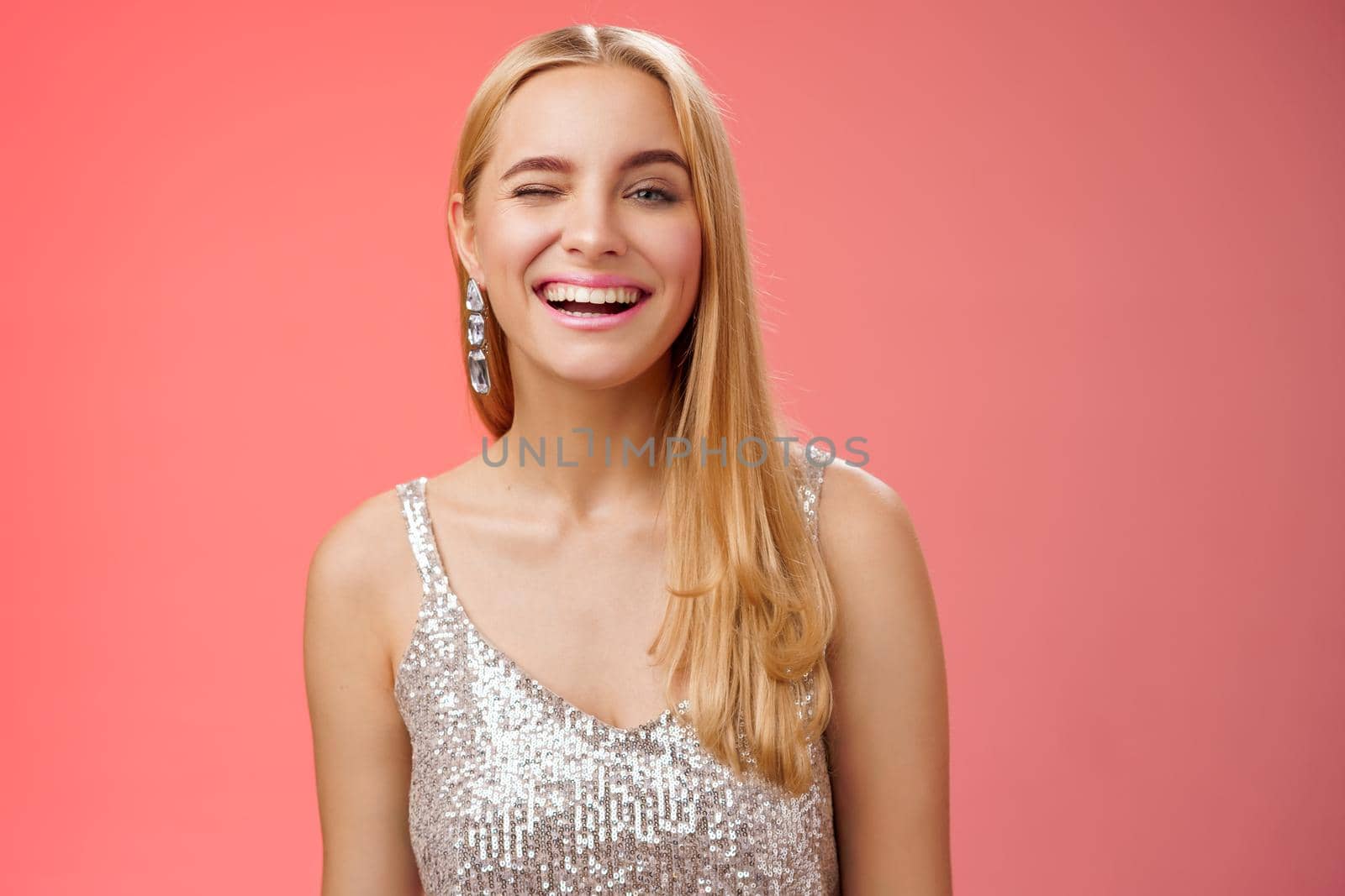 Lifestyle. Carefree joyful charming cheeky blond woman party all night long have fun smiling happily enjoying awesome evening nightclub dancing in silver stylish dress winking sassy camera red background.