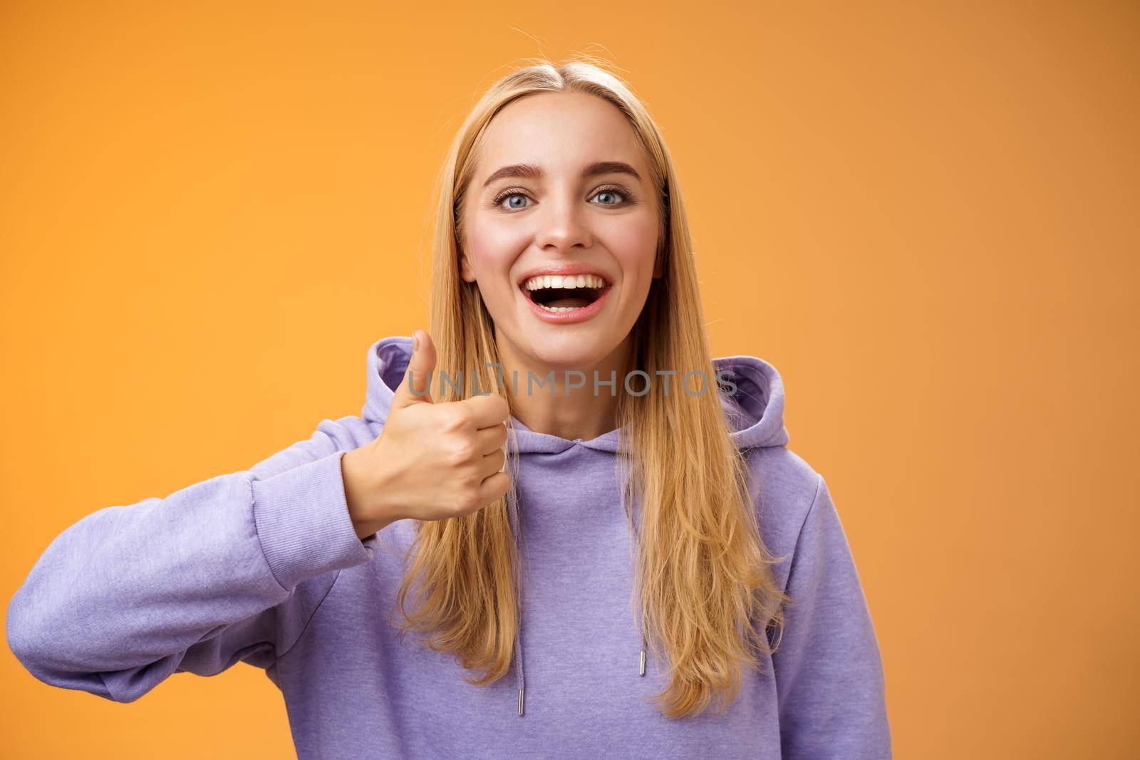 Supportive happy glad young blond attractive woman in hoodie adore perfect good idea show thumbs up approval like gesture smiling broadly accept interesting concept recommend, satisfied by Benzoix