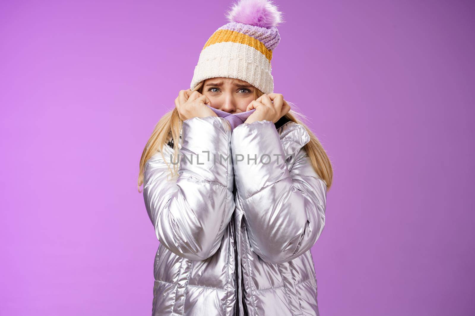 Scared afraid insecure coward girl in cute hat glittering shiny jacket pull cloth face frightened frowning stooping look concerned terrified scared death, standing purple background timid.