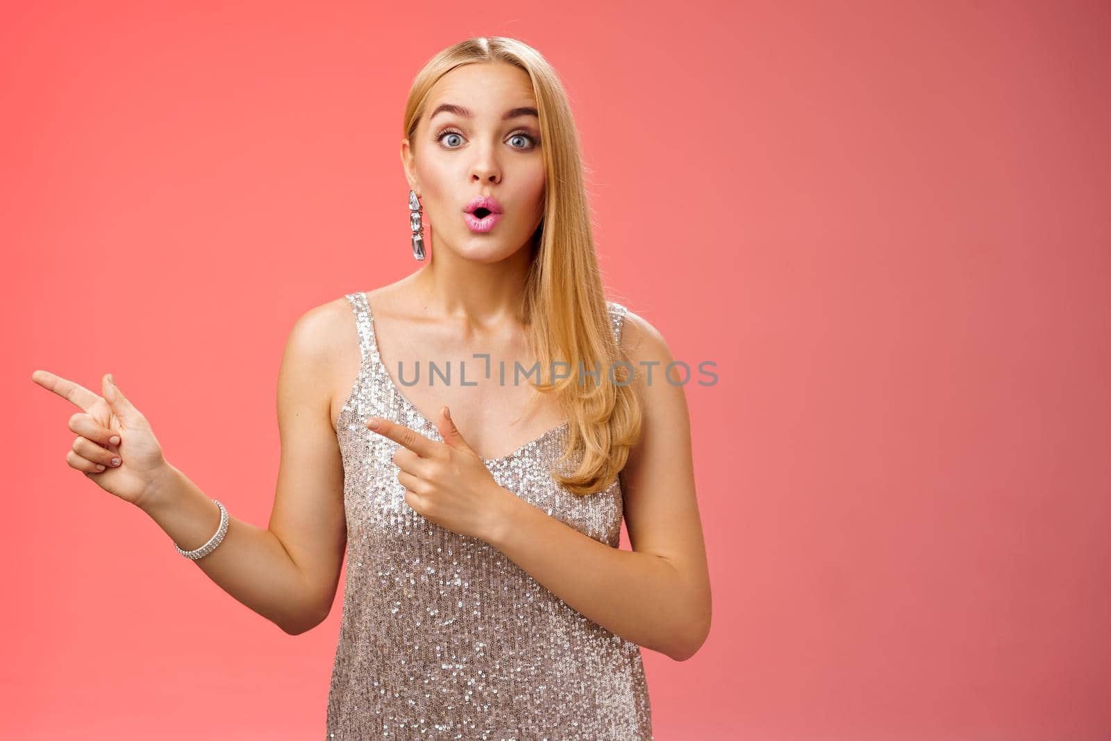 Lifestyle. Intrigued excited attractive tender feminine blond european girl in silver stylish dress pointing left amused talking camera widen eyes thrilled asking boyfriend wanna dance shall go check out promo.