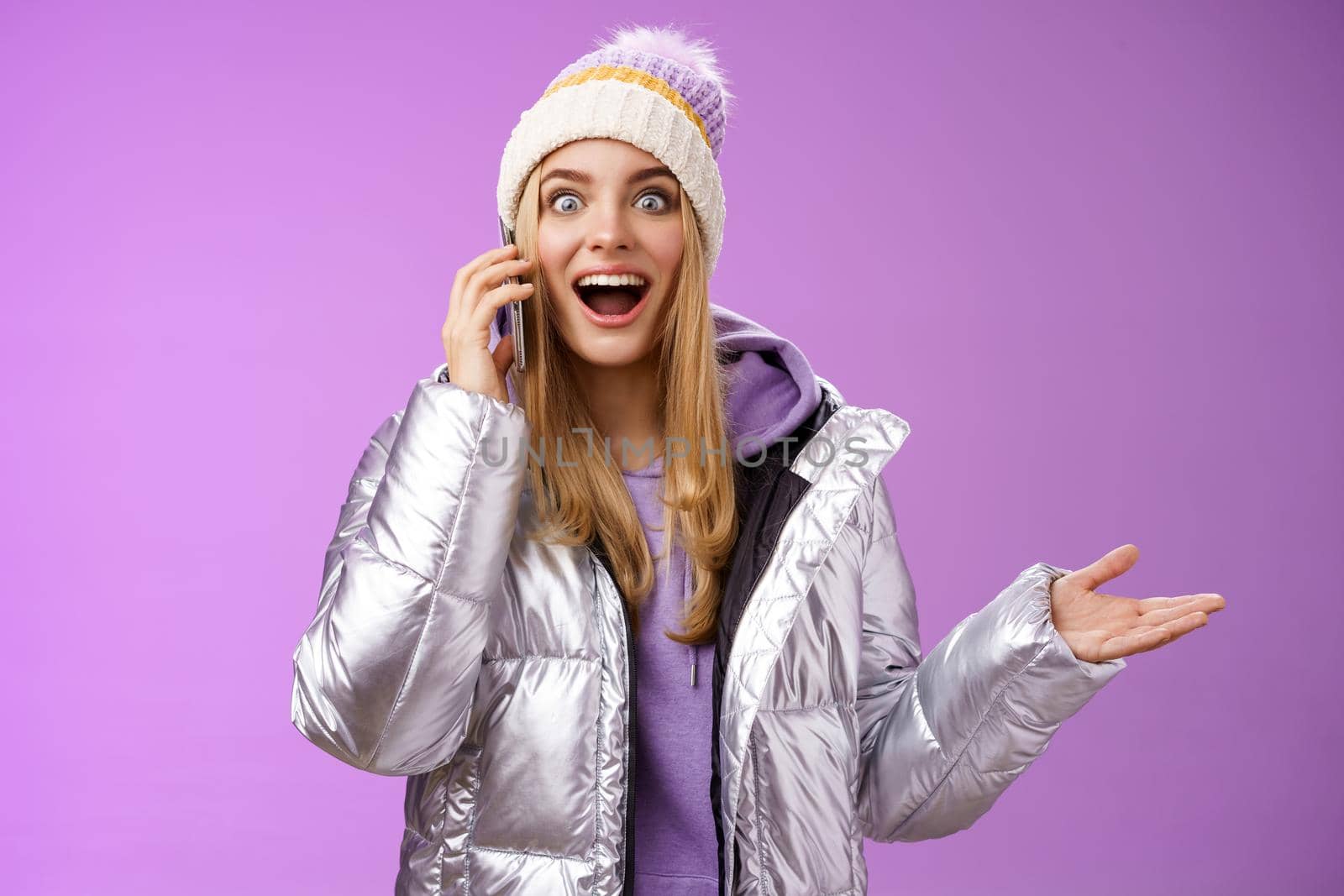 Talkative amused blond girl hearing awesome good news raise hand surprised glad talking smartphone widen eyes satisfied perfect information, standing astonished pleased purple background.
