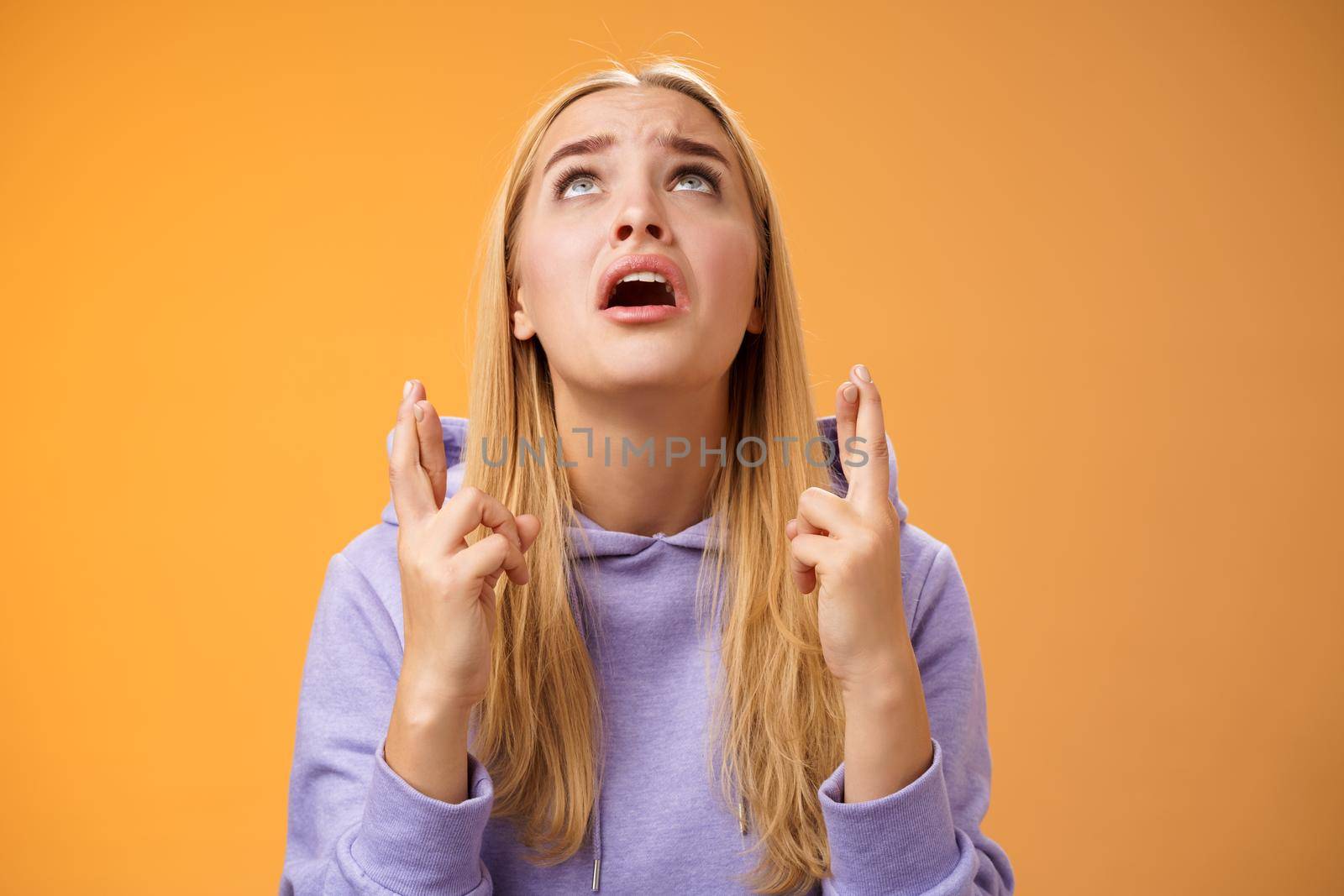 Worried nervous cute blond woman in hoodie begging god help cross fingers good luck supplicating look up skies wanna win anticipating good news anxiously awaiting, orange background.