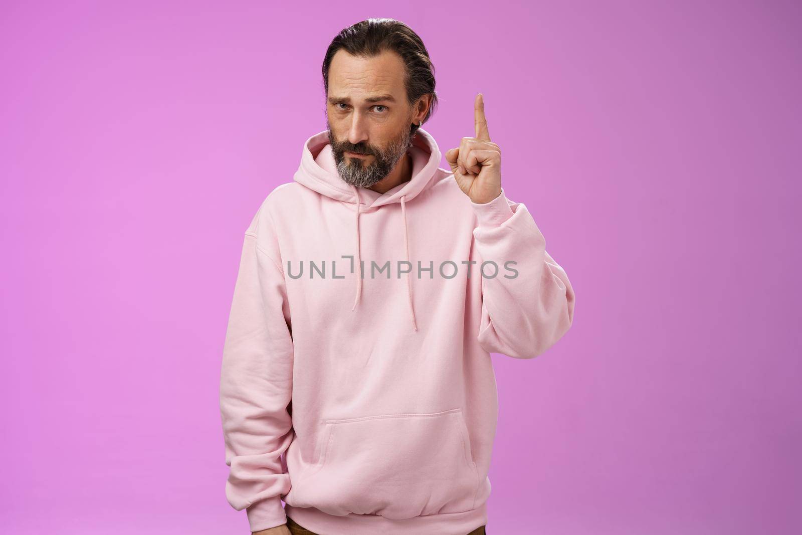 Strict serious-looking stylish bearded father teaching scolding teenage son raising index finger frowning displeased disappointed bad child behaviour, make statement, standing purple background.