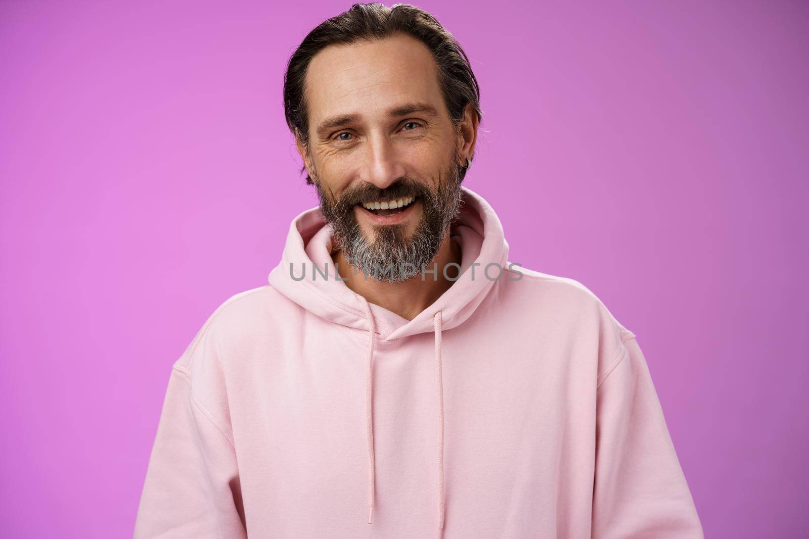 Close-up charming caring friendly-looking european bearded husband talking video chat wife working abroad smiling happy see family standing gladly purple background rejoicing enjoying conversation. Lifestyle.
