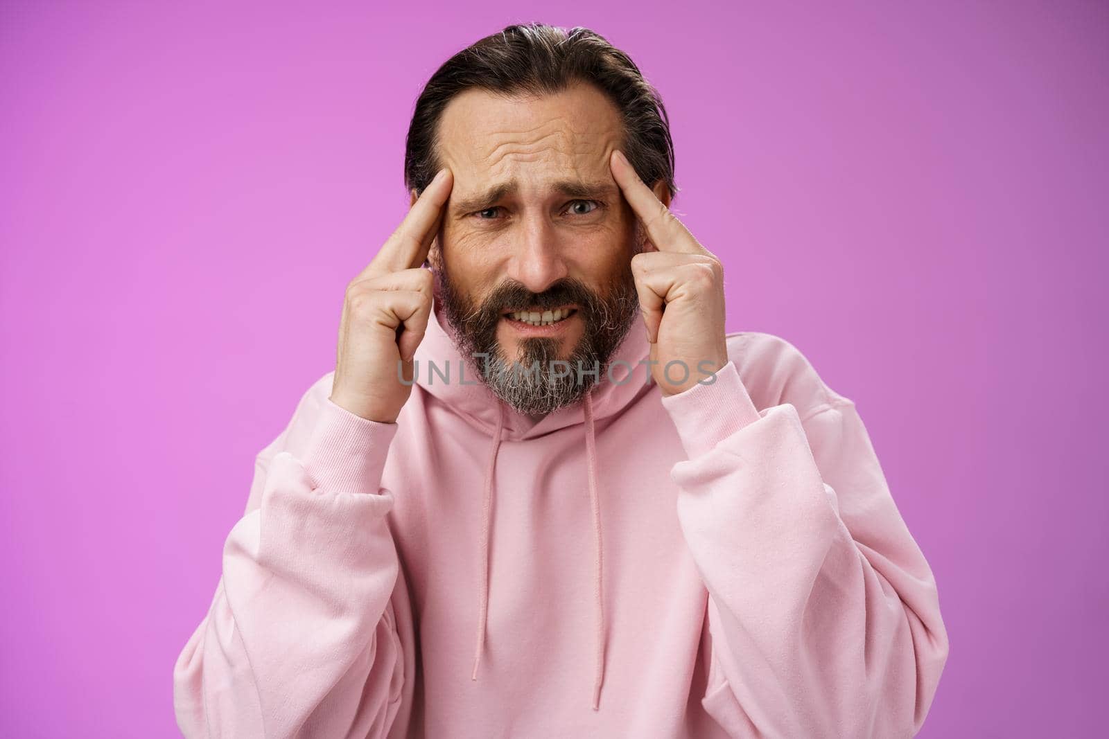 Distressed pressured intense worried mature caucasian man bearded grey hair frowning grimacing thinking hold hands temples bothered cannot make up plan idea, have crisis, purple background by Benzoix