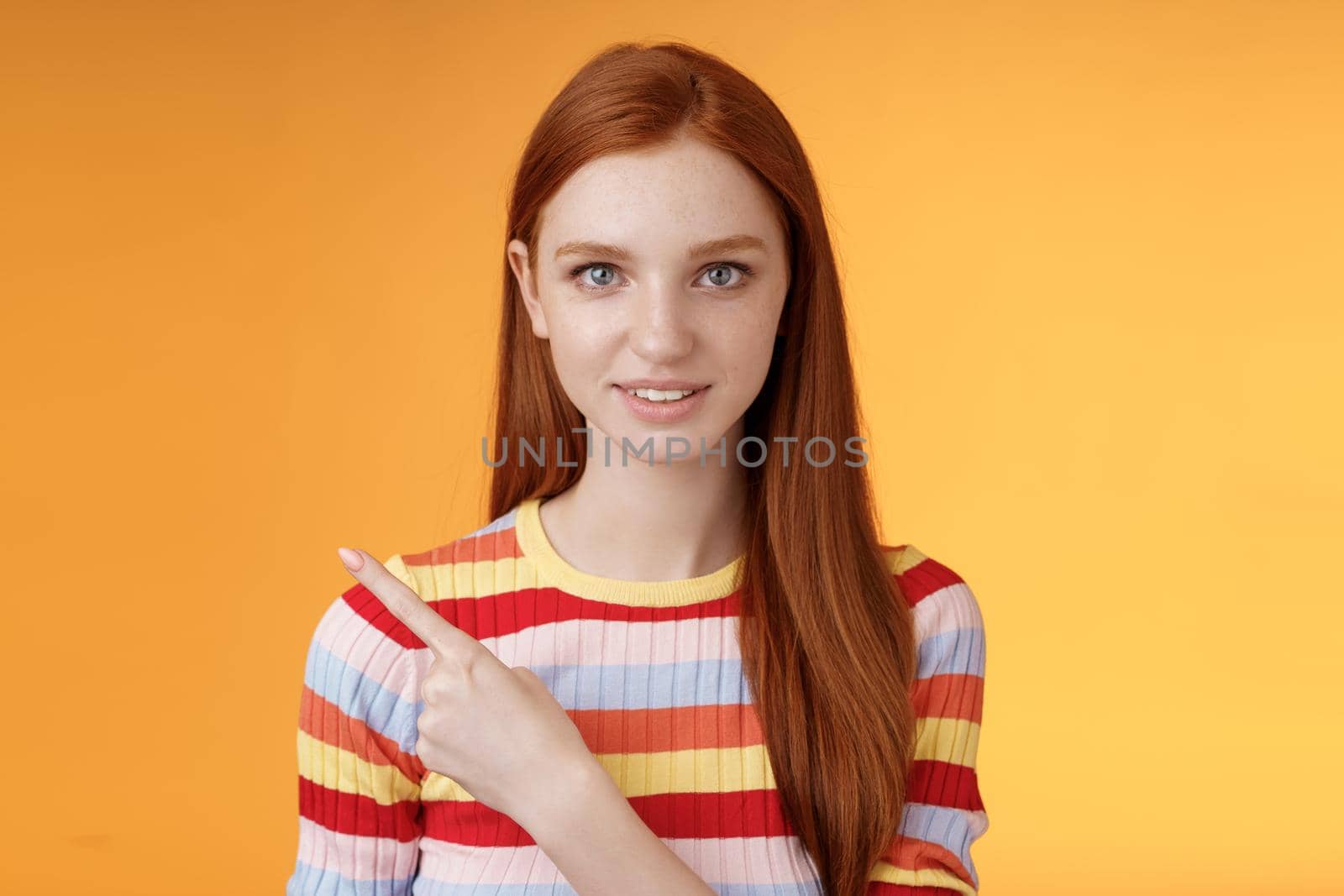 Curious smart female redhead coworker asking friend who was that pointing left index finger look camera thoughtful questioned wanna know answer smiling intrigued standing orange background by Benzoix