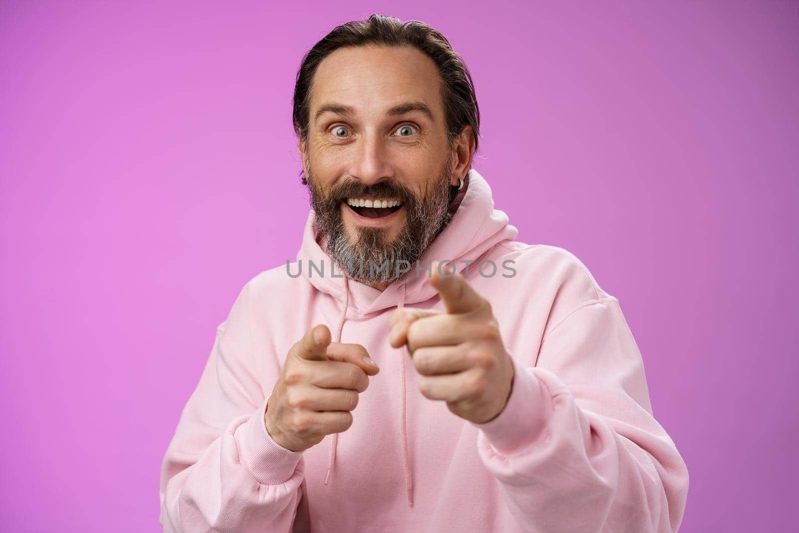 Thrilled energized charismatic happy lucky adult handsome bearded man pointing camera smiling widen eyes gazing impressed see famous person express amazement joy, purple background.