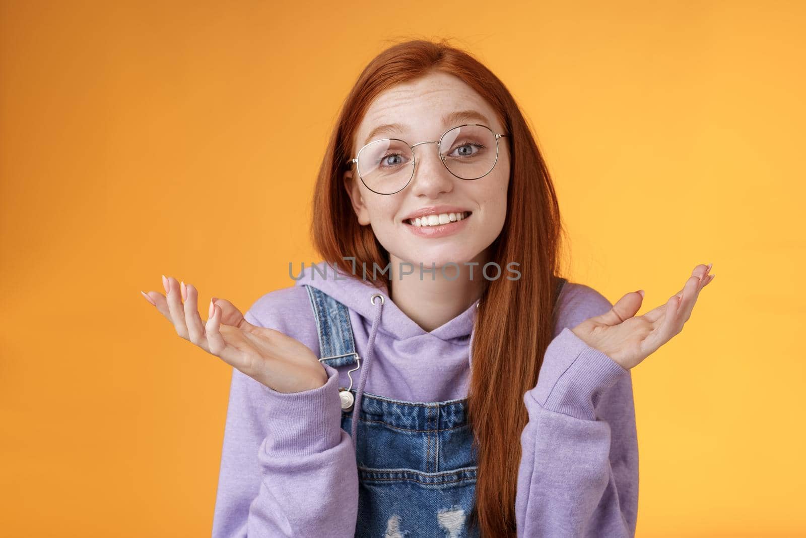 Well no big deal. Attractive silly redhead hipster girl wearing glasses smiling awkward unaware spread hands sideways shrugging confused grinning questioned uncertain what tell, orange background by Benzoix