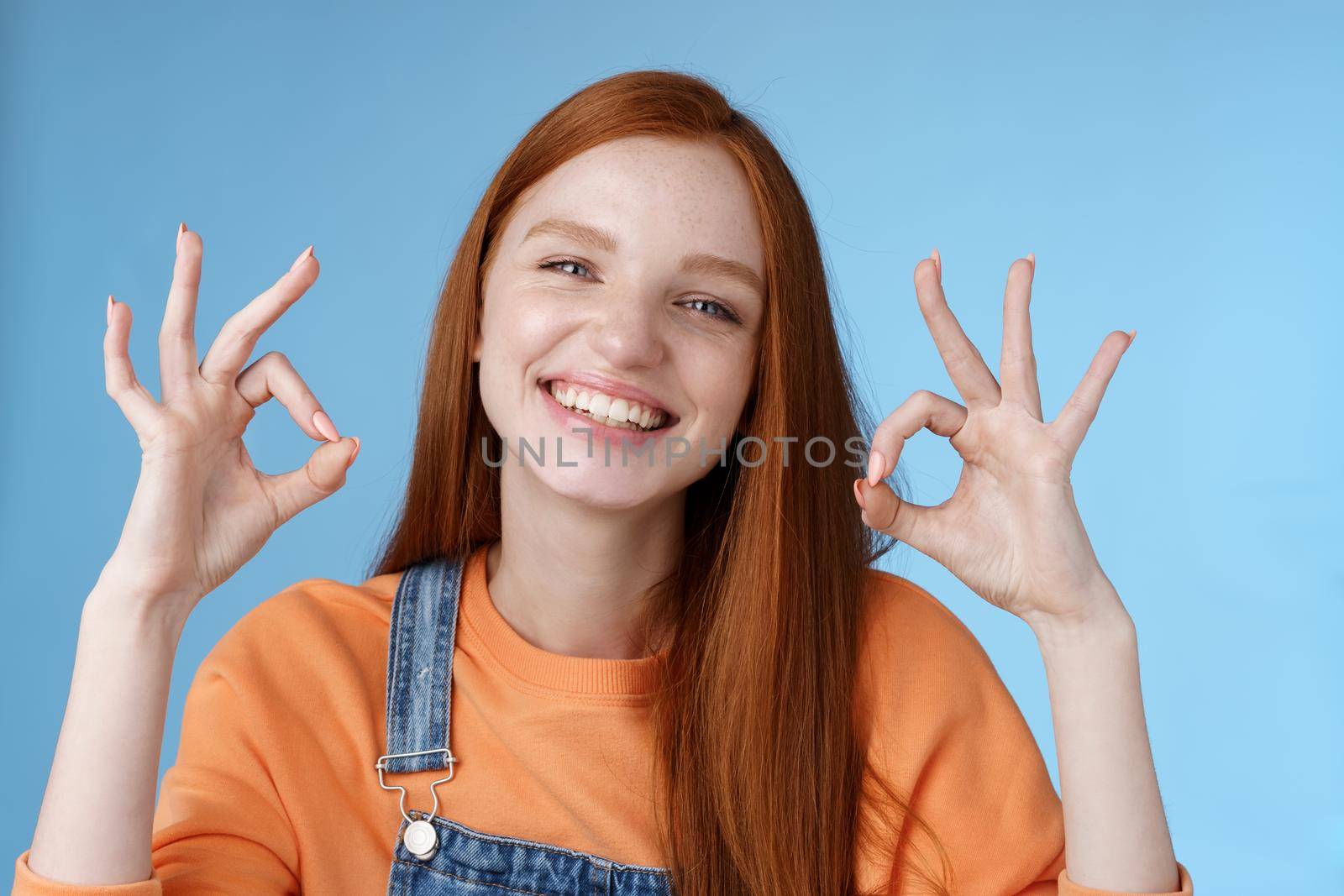 Wellbeing, happiness, perfection concept. Attractive friendly smiling joyful redhead female student show excellent okay ok gestures grinning approval agree awesome concept, satisfied blue background by Benzoix