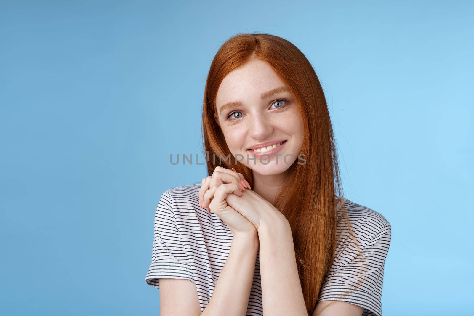 Tender romantic sincere young redhead teenage girl found love look sympathy delight press palms together cute pose smiling happily gazing camera passion lovely grin, blue background.