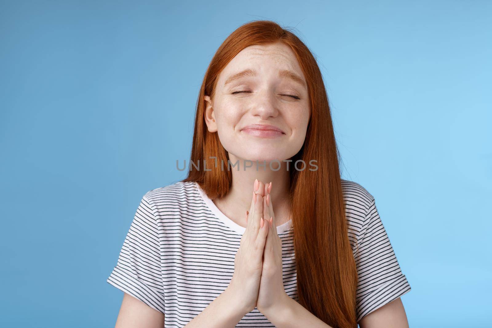 Girl making wish bottom heart willing dream come true press palms together pray supplicating close eyes smiling sincere belief desire fulfill anticipating miracle, standing blue background by Benzoix