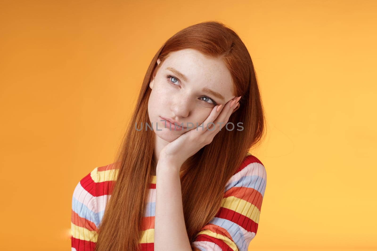 Lonely upset moody cute redhead girlfriend feeling boredom leaning palm look up pouting frowning displeased standing uneasy attend boring meeting, staring uninterested reluctant orange background by Benzoix