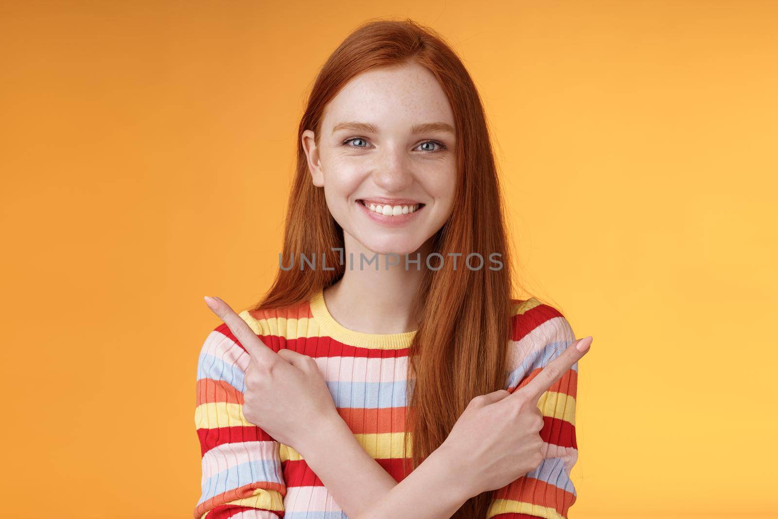 Relaxed carefree confident young helpful redhead girl showing you choices pointing crossed arms left right different directions pick variants present lots opportunities, smiling orange background by Benzoix