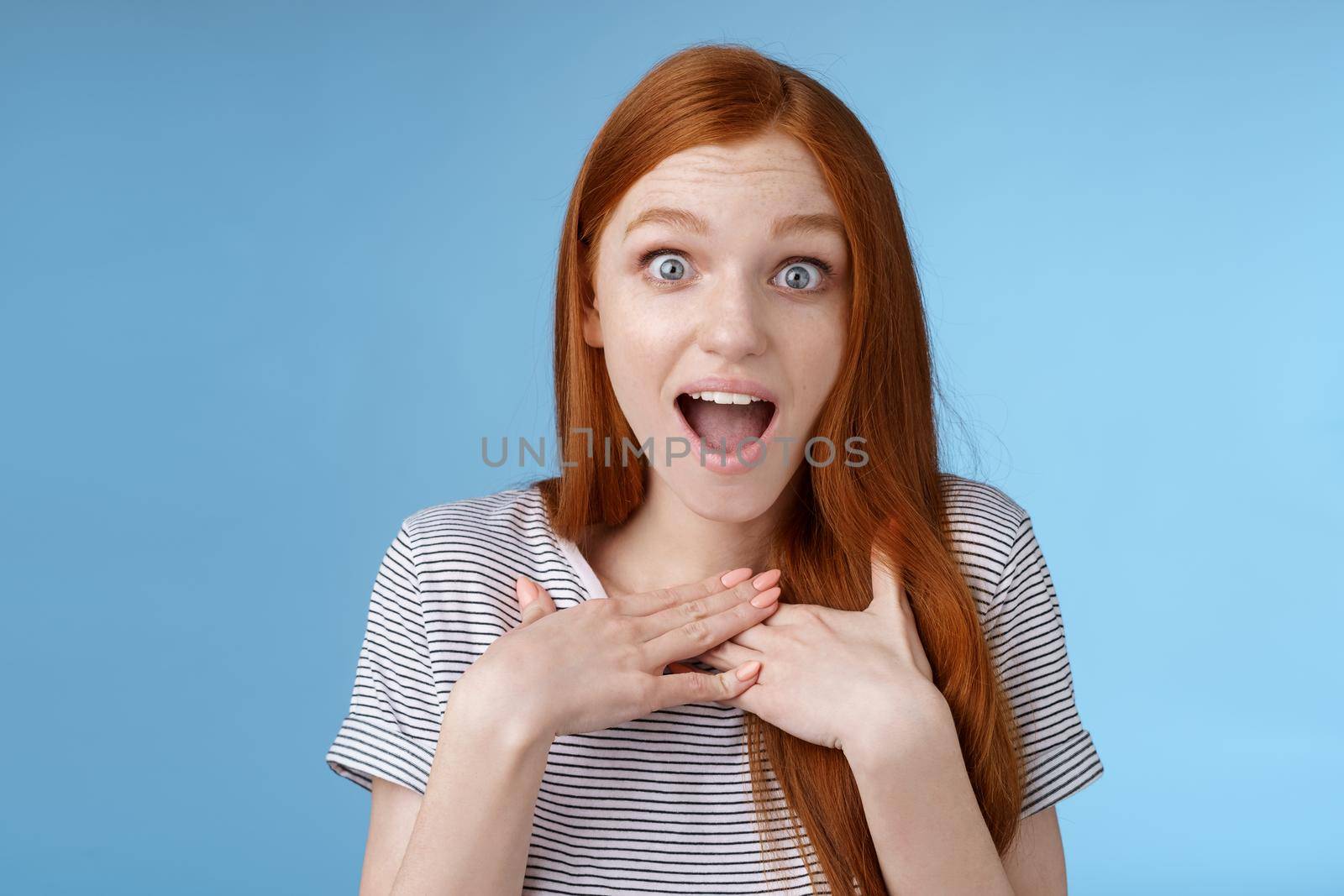 Amused happy grateful european redhead woman gasping drop jaw joyfully press palms chest thankful staring surprised incredible cool gift receive awesome proposal standing blue background by Benzoix