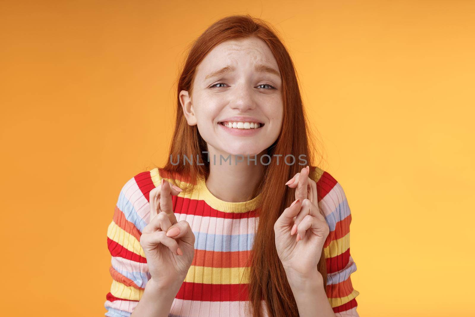 Attractive redhead hopeful girl anticipating good news excitement thrill cross fingers good luck smiling broadly praying wish come true good results receive prize, standing orange background desire.