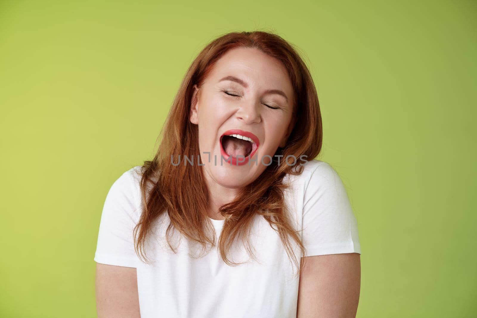 Lazy weekends finally time sleep. Cheerful redhead middle-aged 50s woman yawning satisfied close eyes feel sleepy wake up early morning wanna take nap stand green background watching boring film.