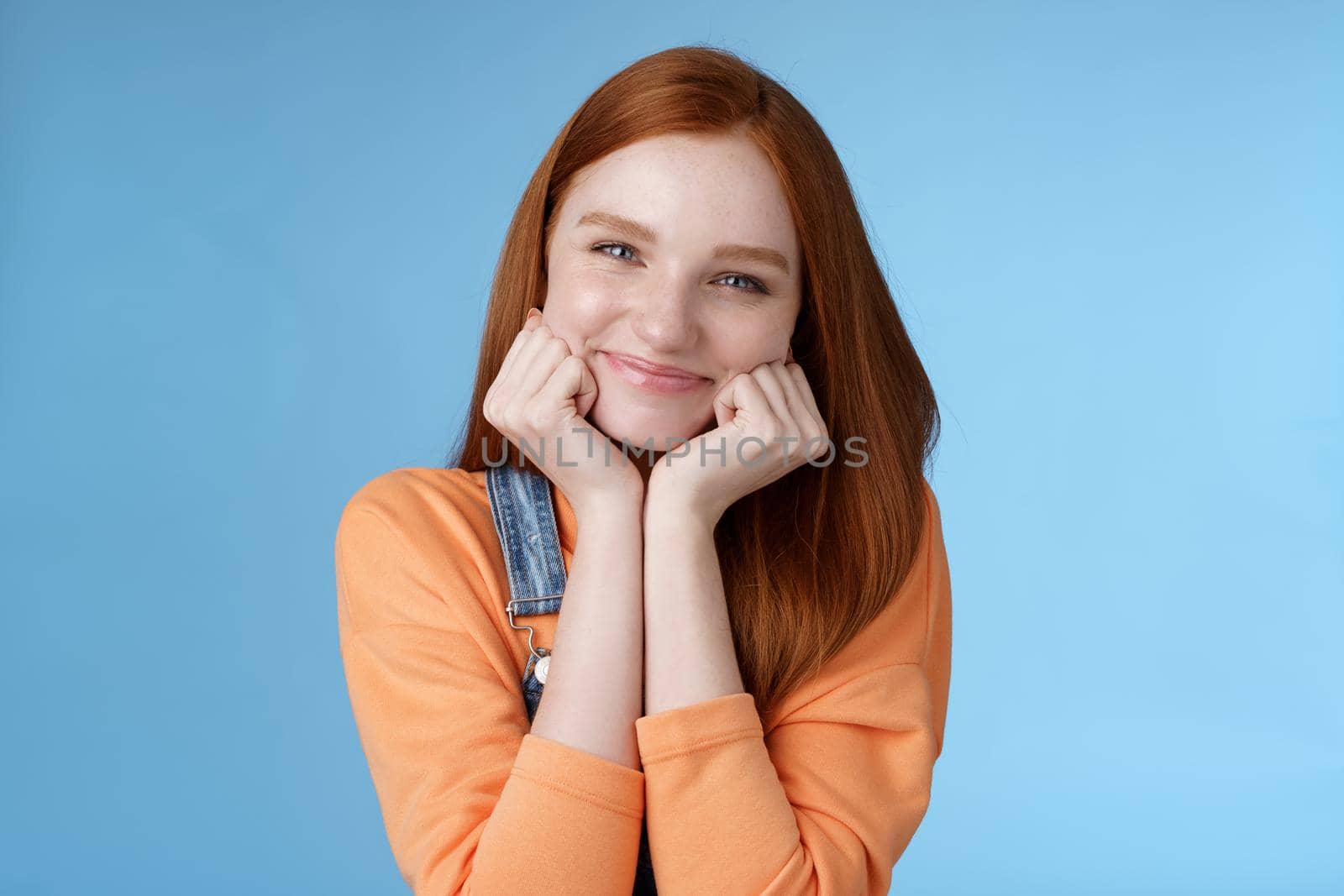 Tenderness, wellbeing, beauty conept. Attractive young ginger girl pure skin blue eyes lean palms silly smiling camera look amused enthusiastic listen interesting stories gladly, blue background by Benzoix