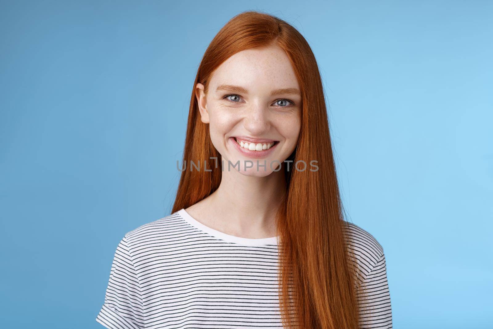 Pleasant reliable sincere good-looking redhead female freelancer college student make confident professional impression smiling broadly assertive helpful standing blue background self-assured.