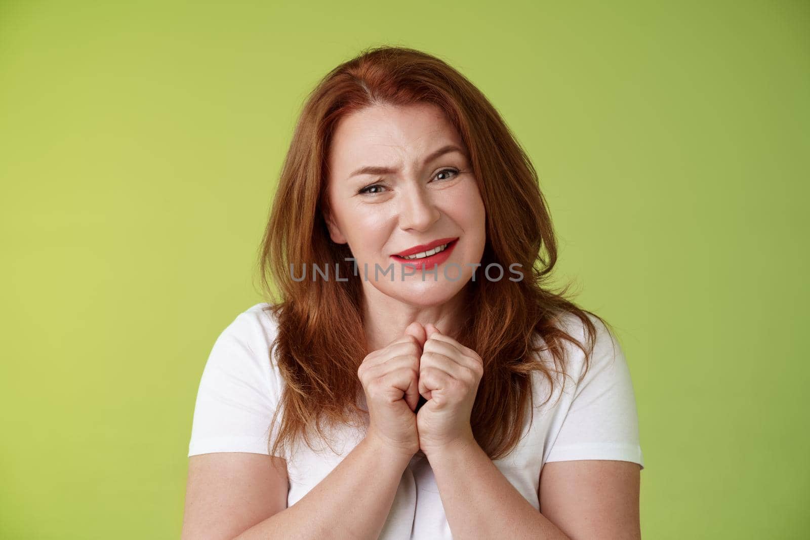 Silly touched tender redhead charmed middle-aged woman sighing gladly gaze admiration delighted press hands together heartwarmed fascinated look grateful lovely camera green background.