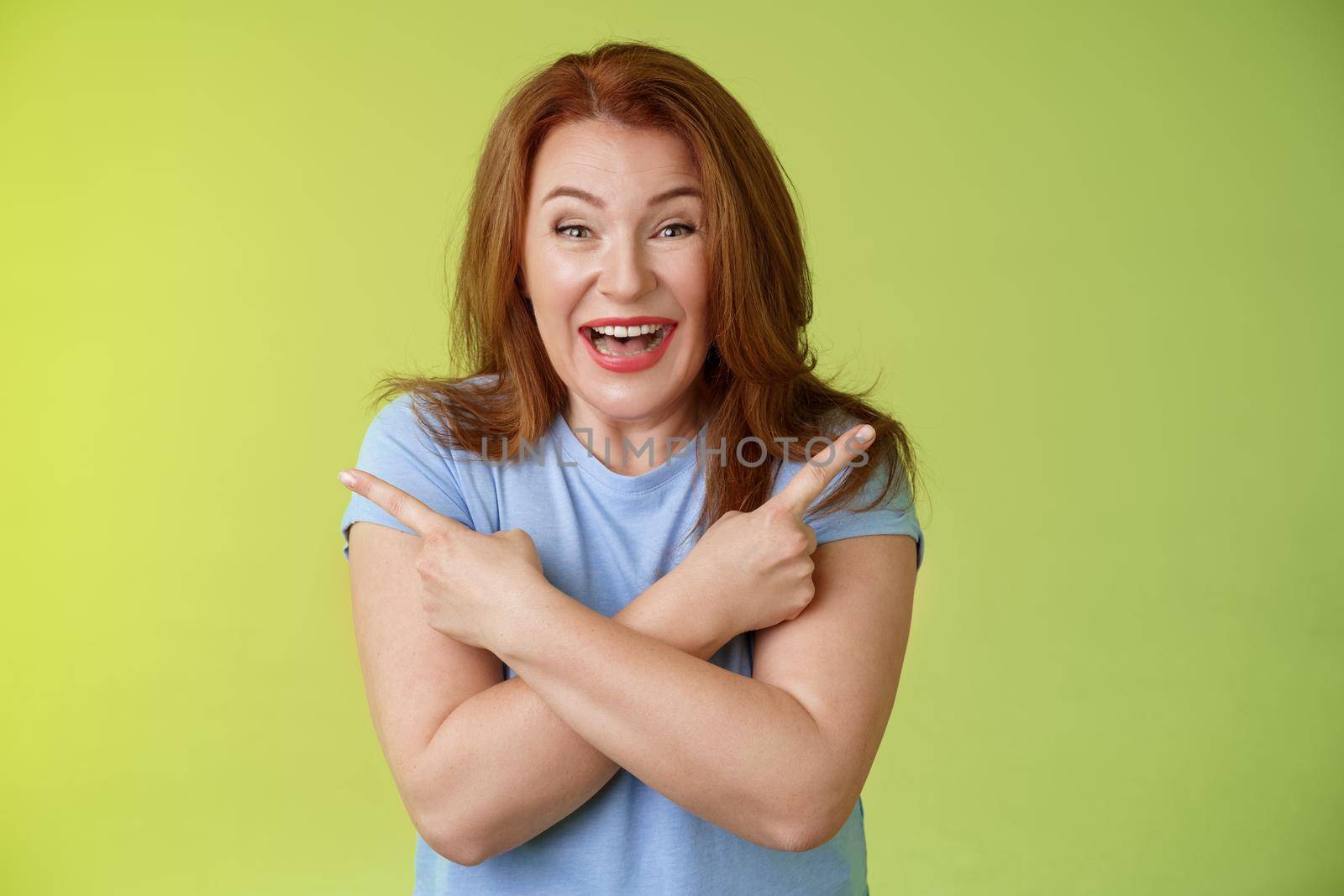 Lifestyle Concept - Happy carefree entushiastic redhead funny mature female. having fun positive attitude cross arms body pointing sideways show left right products laughing happily like both choices green background.