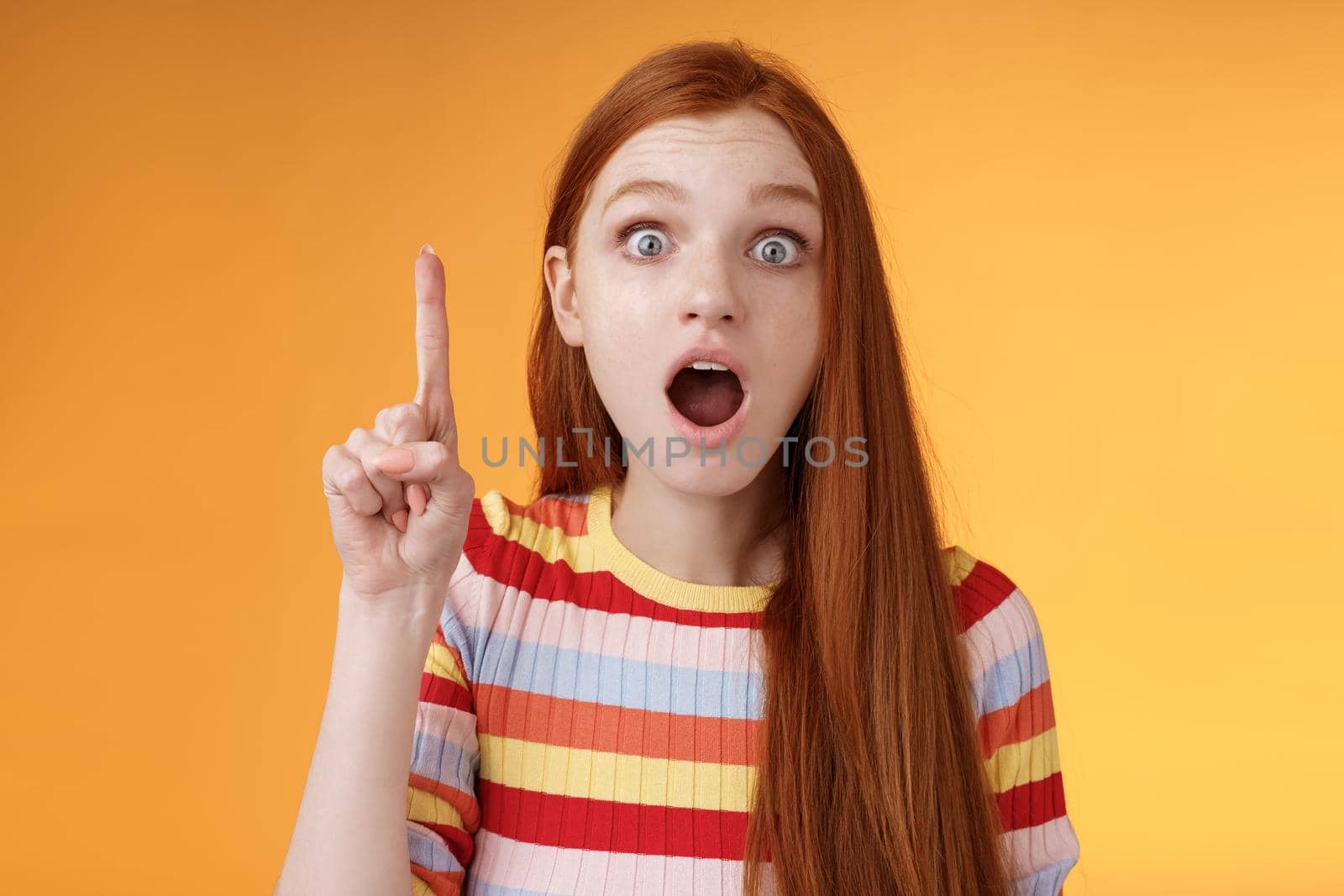 Got idea hurry listen. Excited young emotional redhead female coworker raising index finger eureka gesture open mouth wide eyes shocked thrilled telling excellent plan thinking-up solution.