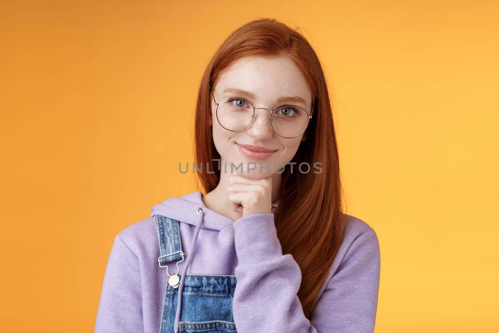 Confident happy relaxed european redhead skillful young female entrepreneur glasses establish startup smiling delighted look pleased result touch chin thoughtful smart, orange background by Benzoix