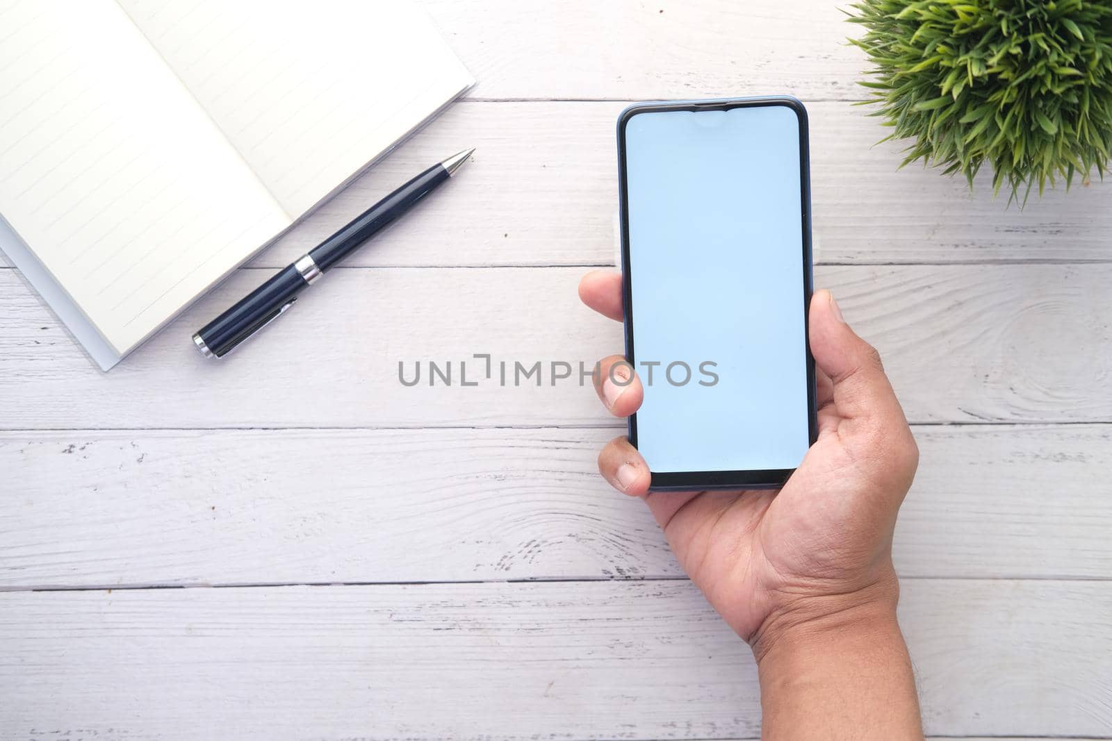 Top view of man hand holding smart phone with empty screen on office desk .