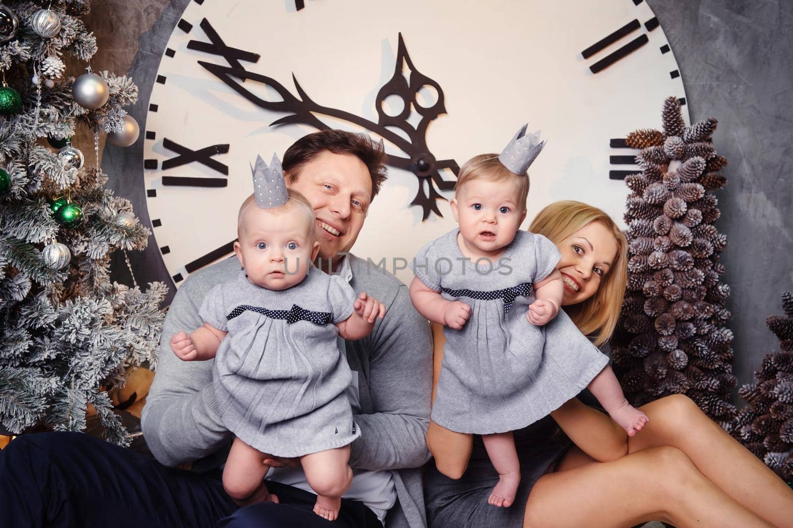 A happy big family with twin children in the New Year's interior of the house against the background of a large clock.