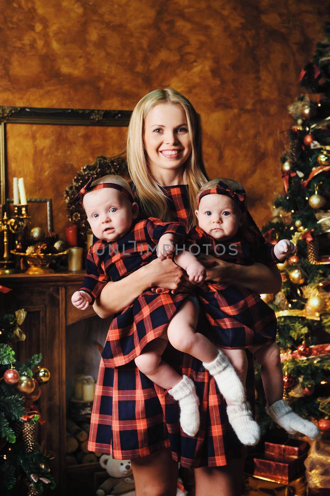 A happy mother with her twin children in the New Year's interior of the house on the background of a Christmas tree.