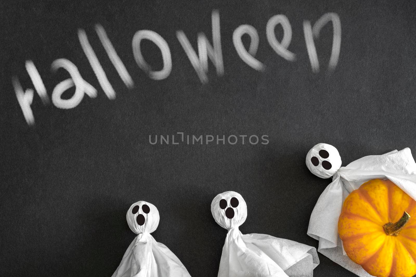 Three ghosts and pumpkin, black background, inscription helloween. Top view. Copyspace. Halloween Concept