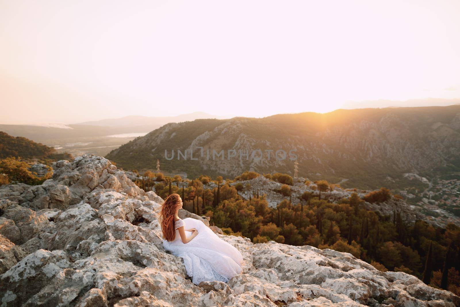 The bride in tender wedding dress sits on the rock on Mount Lovcen and looks at the Bay of Kotor . High quality photo
