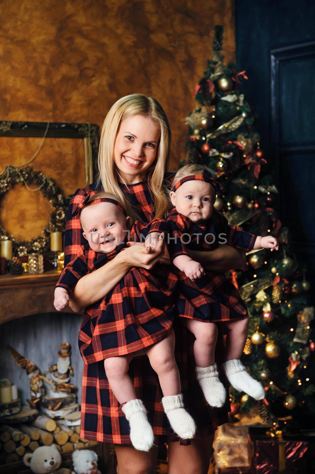 A happy mother with her twin children in the New Year's interior of the house on the background of a Christmas tree by Lobachad