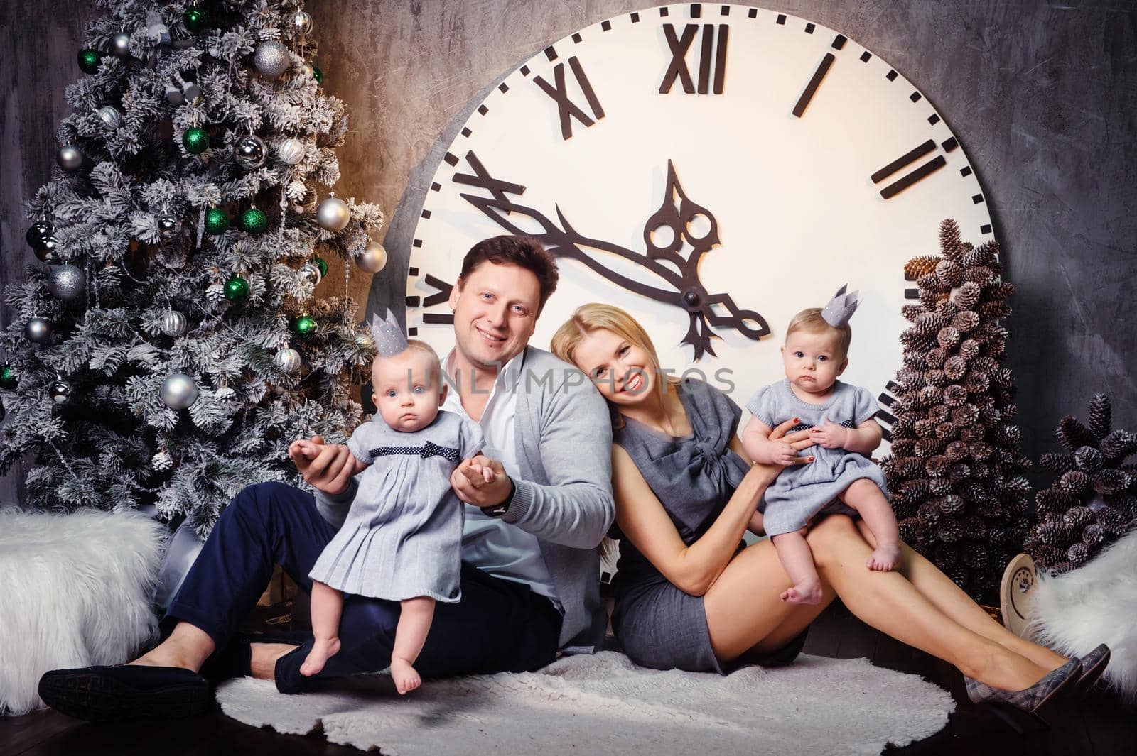 A happy big family with twin children in the New Year's interior of the house against the background of a large clock.