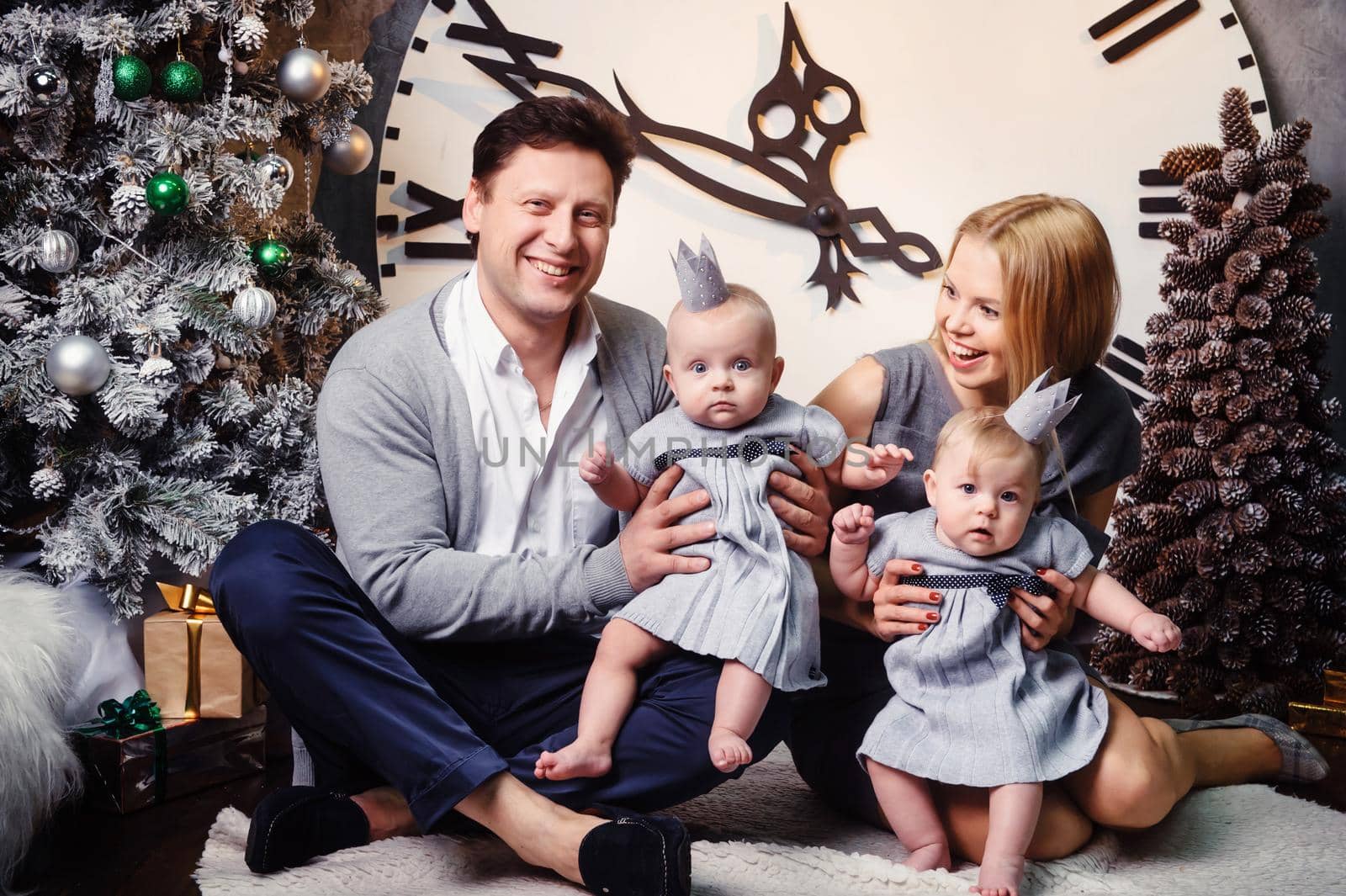 A happy big family with twin children in the New Year's interior of the house against the background of a large clock.