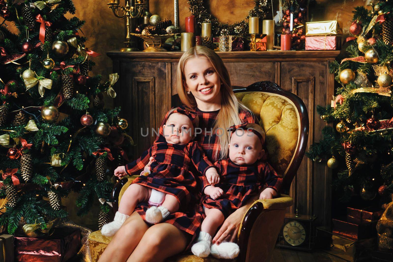 A happy mother with her twin children in the New Year's interior of the house on the background of a Christmas tree by Lobachad