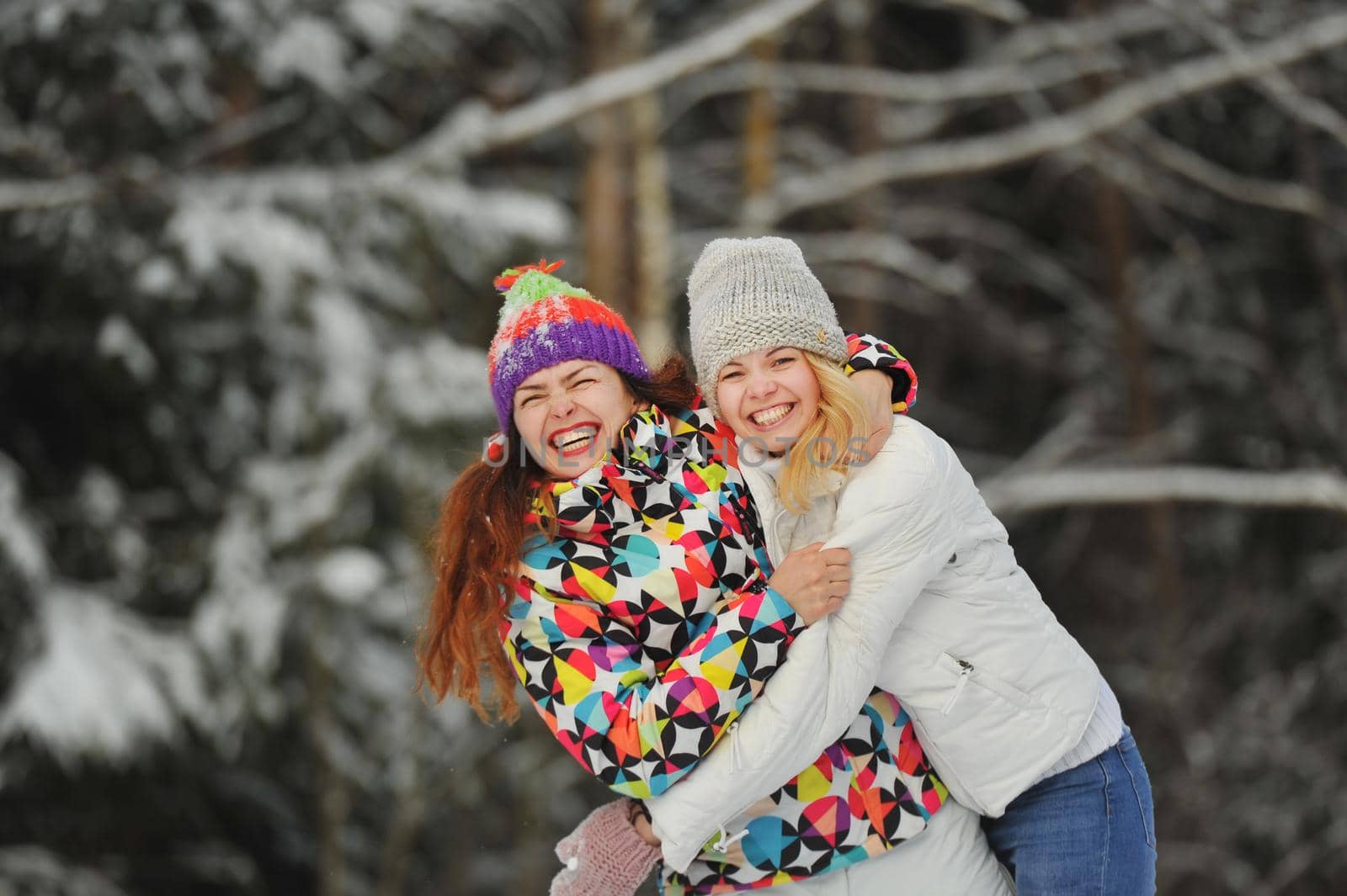 Two girls in the winter forest emotionally hug and smile.Happy women hug and Express joy by Lobachad