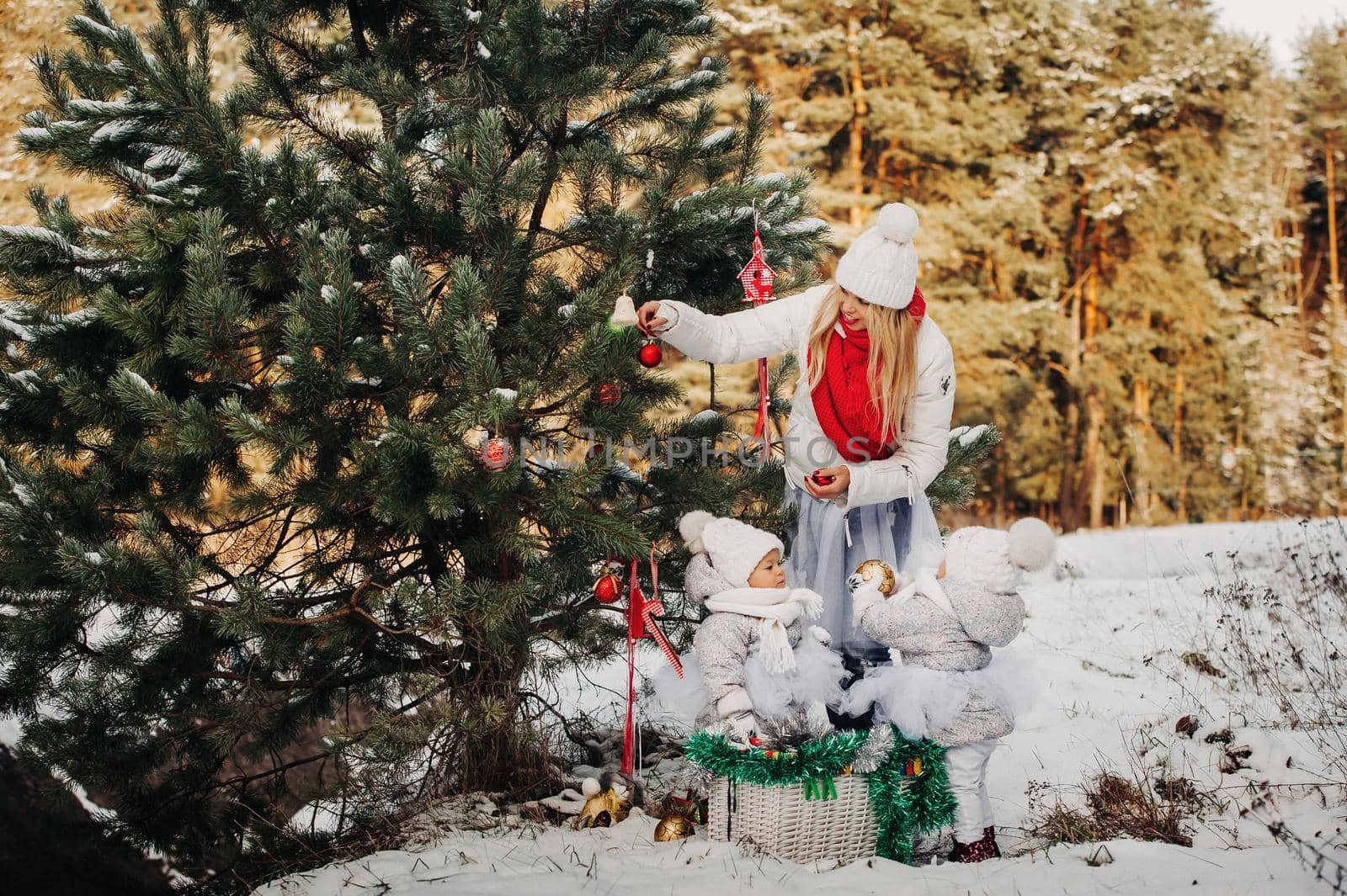 Mom and children at the Christmas tree on the street decorate it.