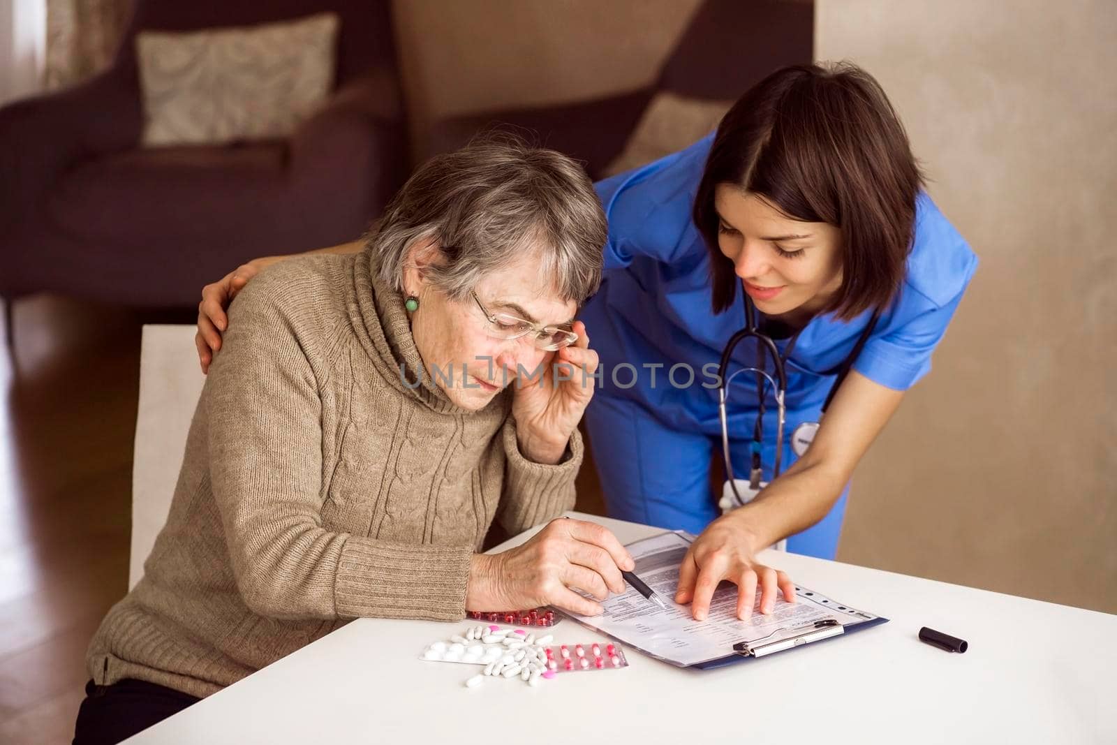An elderly gray-haired woman with glasses reads a health insurance contract and signs it. The document is offered by a young woman to a doctor, a nurse with a stethoscope. Safety, care and medicine.
