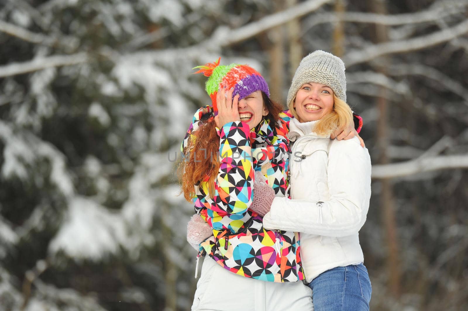 Two girls in the winter forest emotionally hug and smile.Happy women hug and Express joy by Lobachad