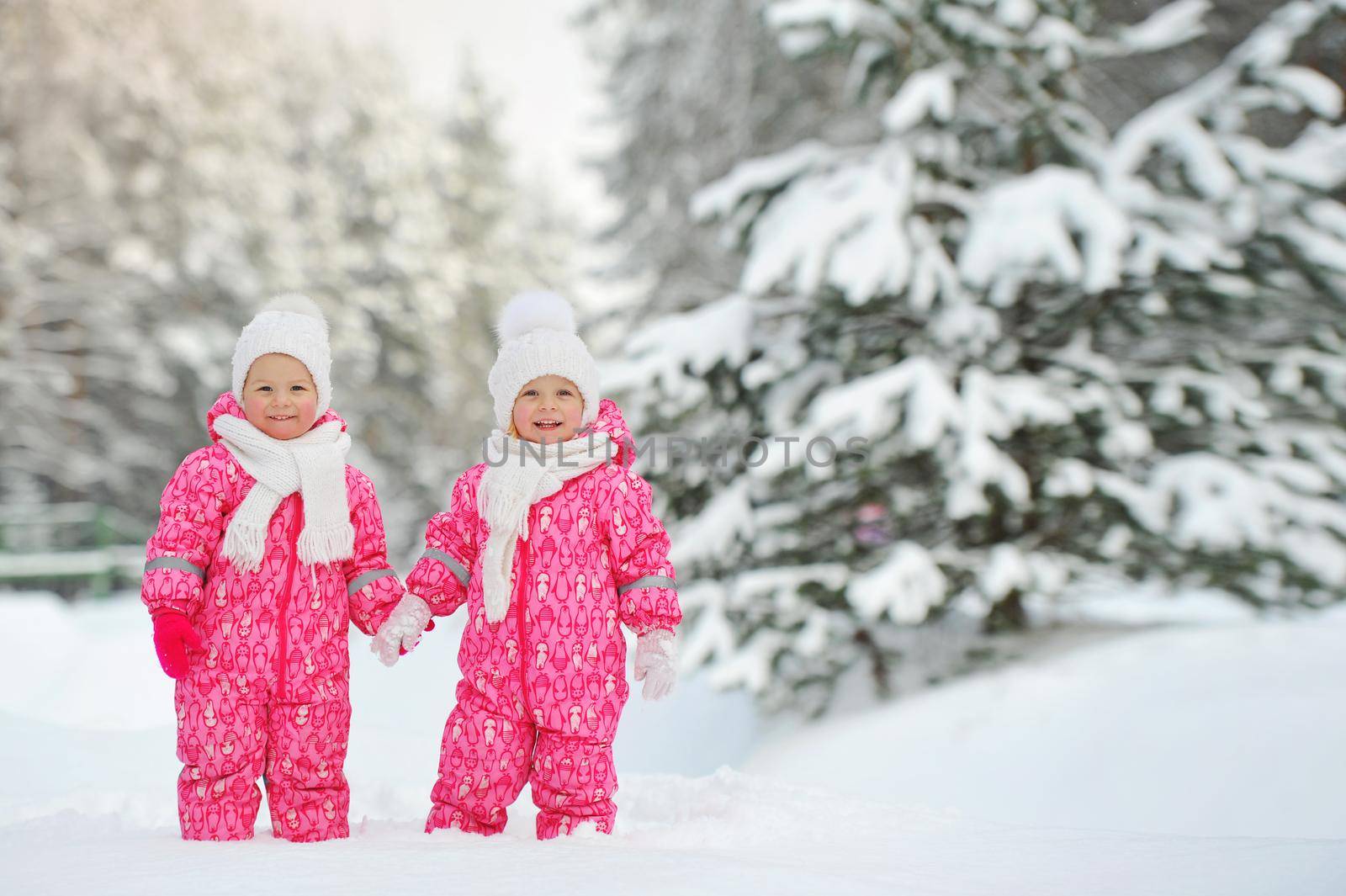 Two little twin girls in red suits stand in a snowy winter forest by Lobachad