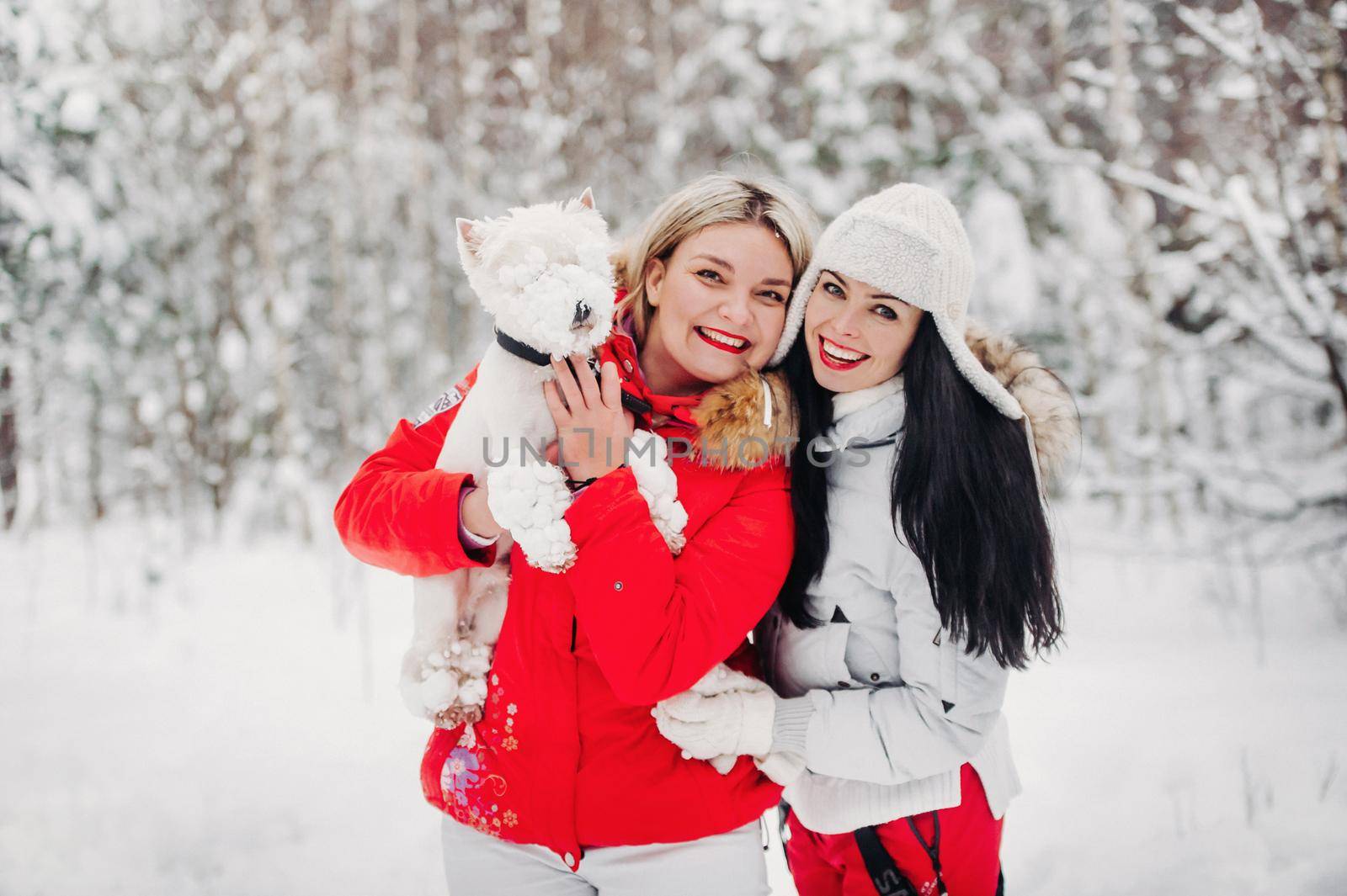 Portrait of two girls with a dog in a cold winter forest. A girl holds a dog in her arms in a snowy winter forest.