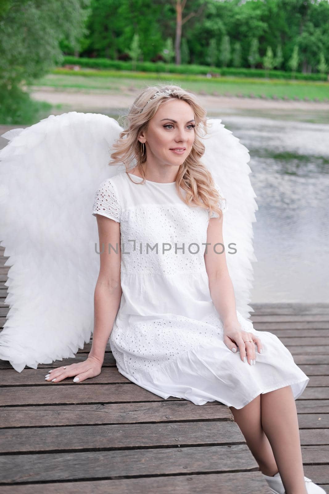 beautiful angel in white dress. Amazing blond woman with long curly hair and white wings