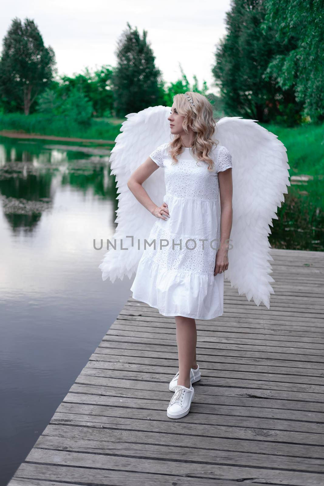 charming blonde with white angel wings standing by the water. beautiful woman in angel costume. goddess by oliavesna