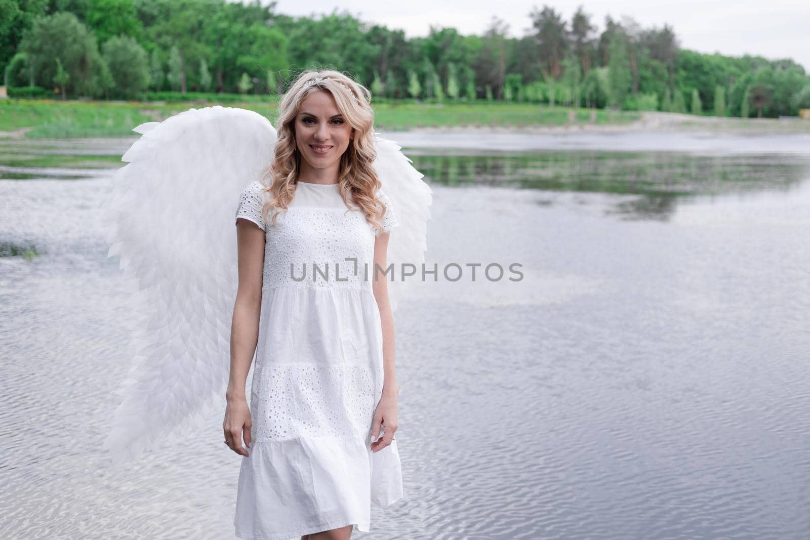 beautiful angel in white dress. Amazing blond woman with long curly hair and white wings