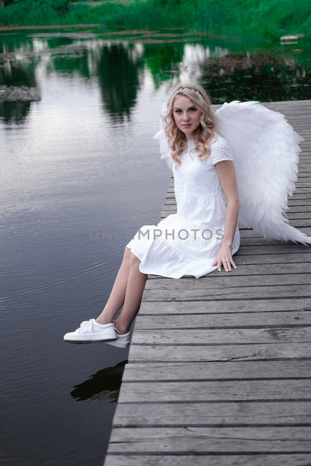 charming blonde with white angel wings standing by the water. beautiful woman in angel costume. goddess by oliavesna