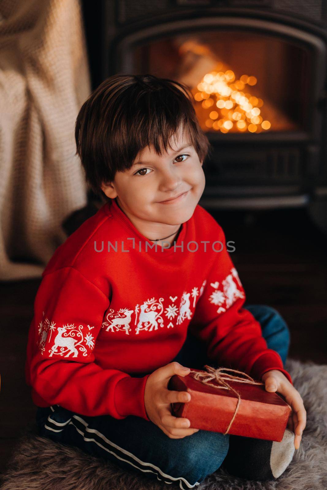 portrait of a smiling boy with a gift in his hands near the fireplace at home.