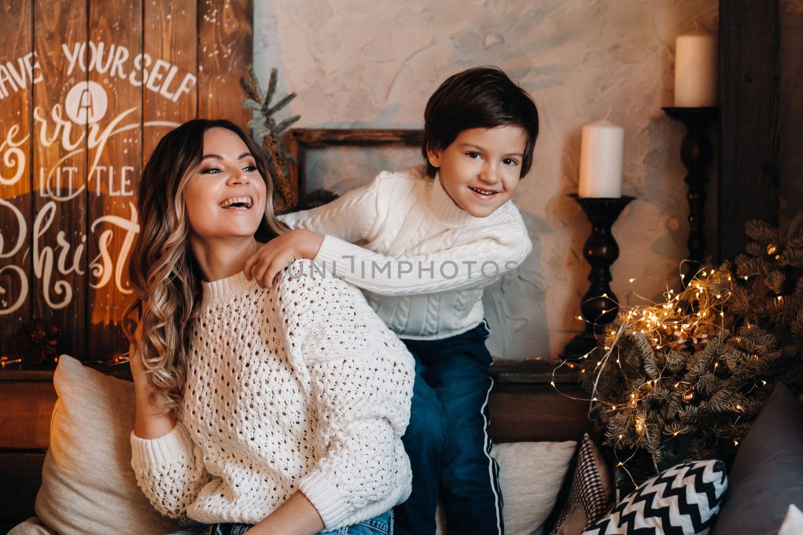 Mom and son are sitting at home on the couch before the new year and smiling together by Lobachad