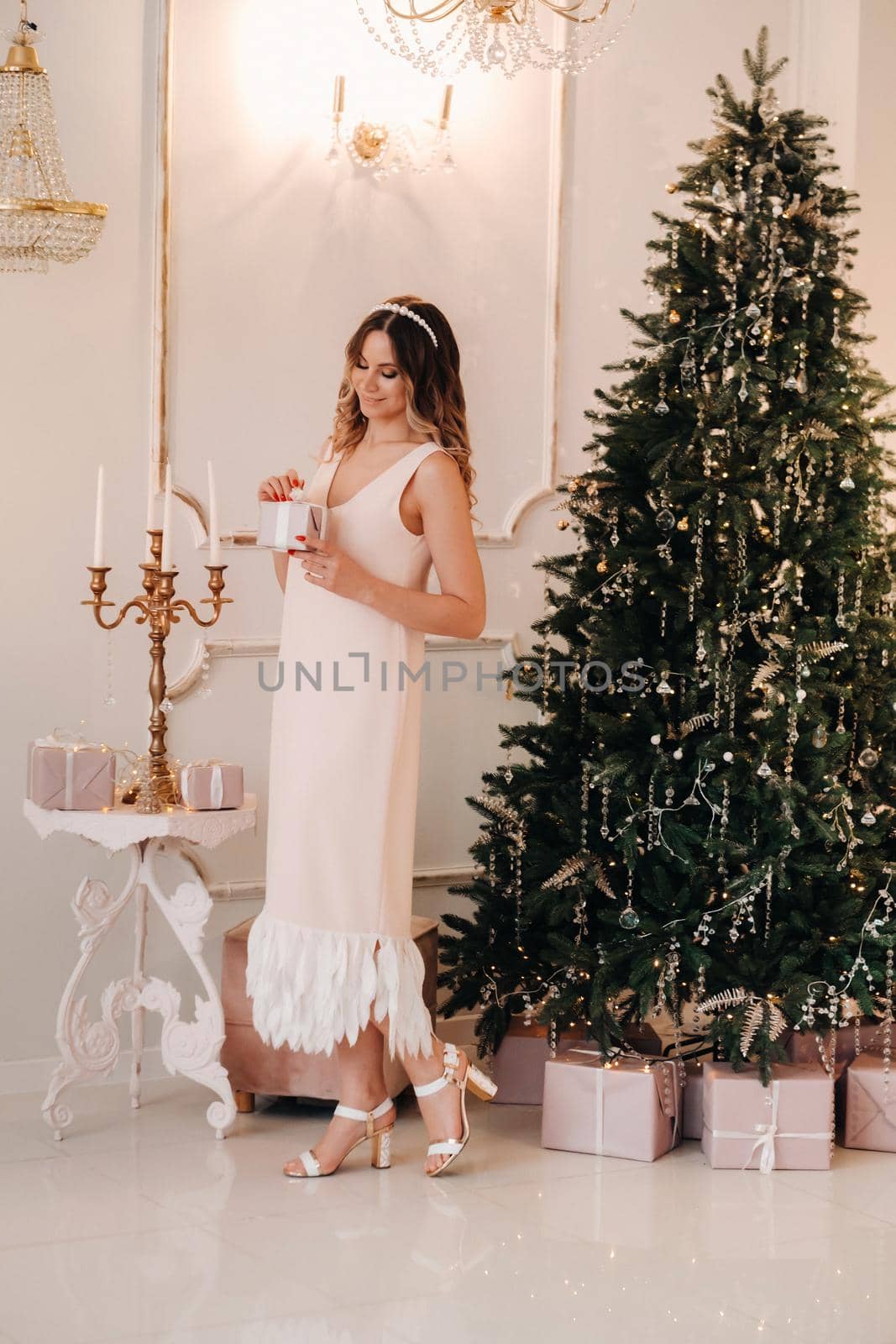 portrait of a smiling girl in a pink dress with a Christmas gift in her hands near the Christmas tree at home.